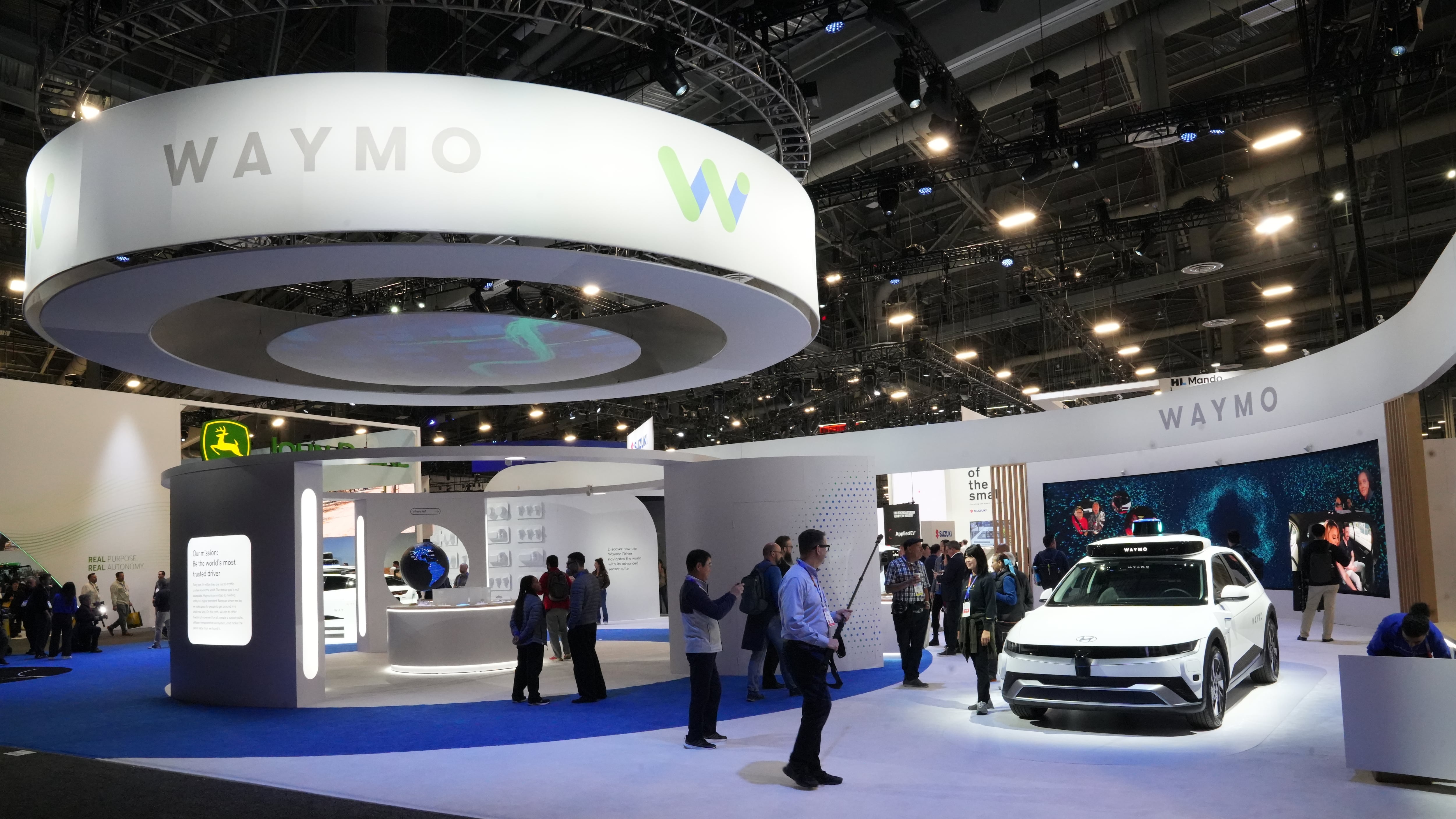A white car surrounded by onlookers at a technology show display.